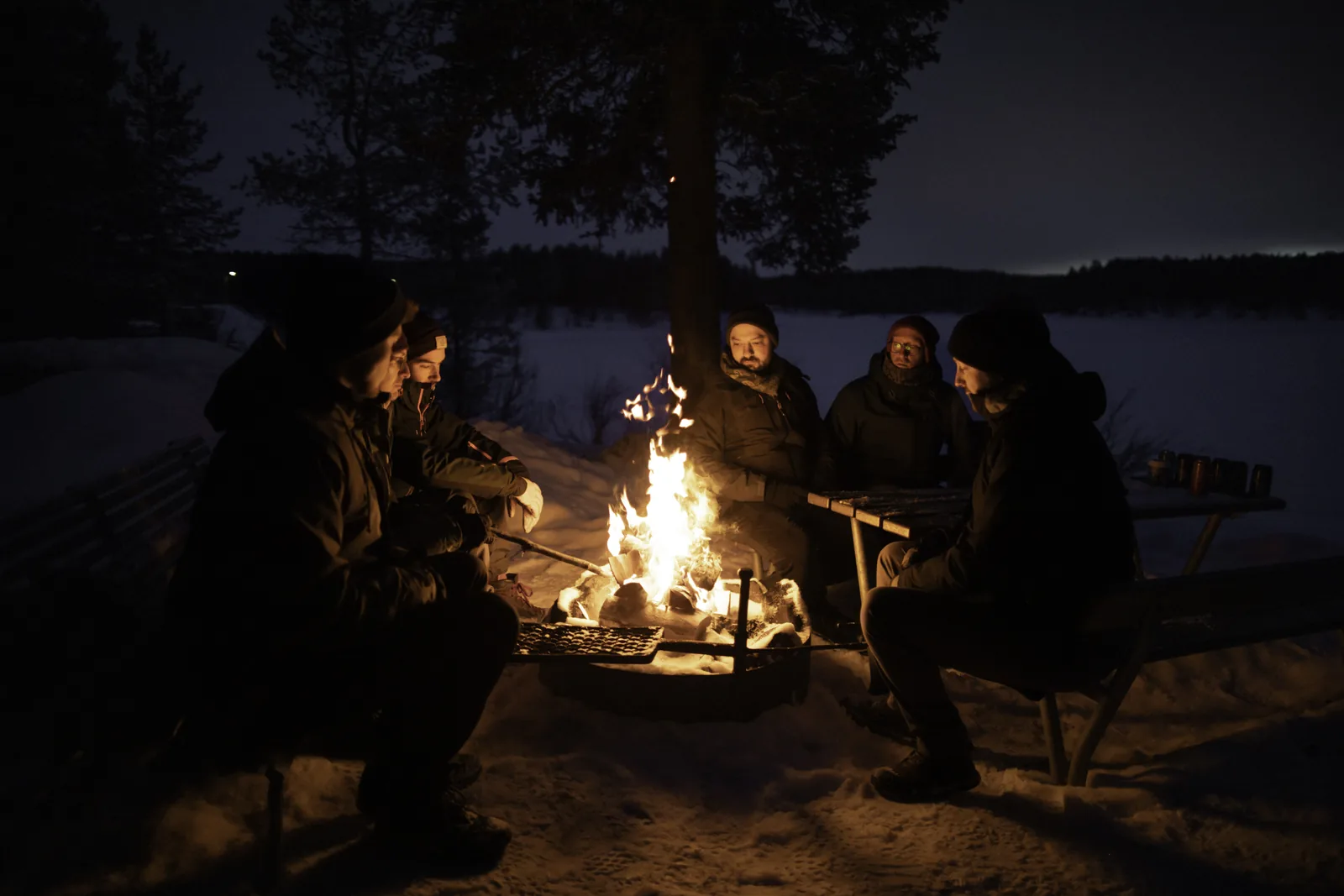 Guests warming up around an open fire by the lake during an aurora chase