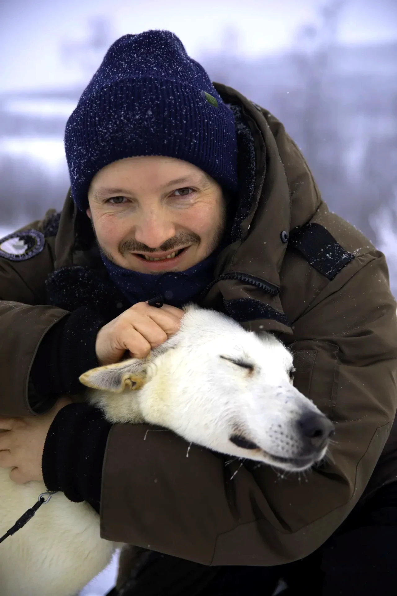 A guest cheek to cheek with a husky after dog sledding