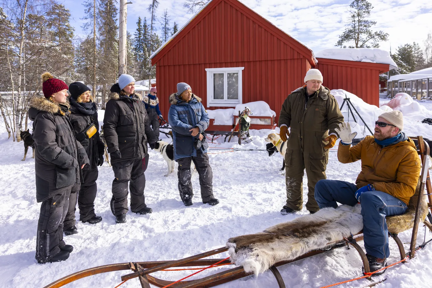 Guests gathered by a red wooden cabin out in the snow near Kiruna