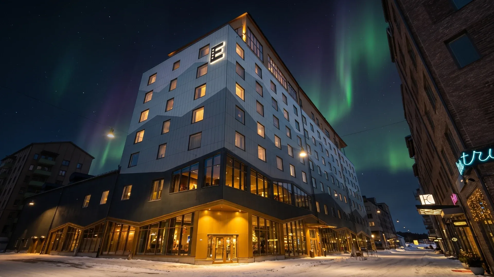 Elite Hotel Frost lit up at night in central Kiruna, with the northern lights above the rooftops