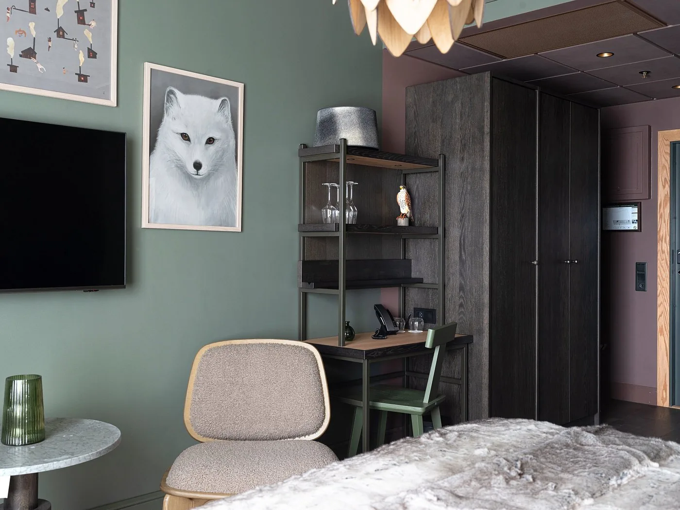 Desk, armchair and wardrobe in a green-walled room at Elite Hotel Frost, with a fur throw on the bed
