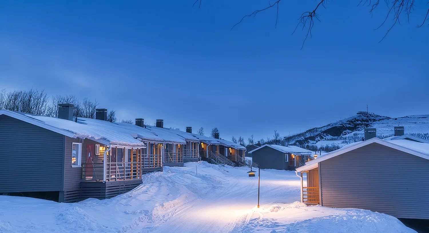 A row of snow-covered wooden cabins at Camp Ripan under a deep blue Arctic twilight