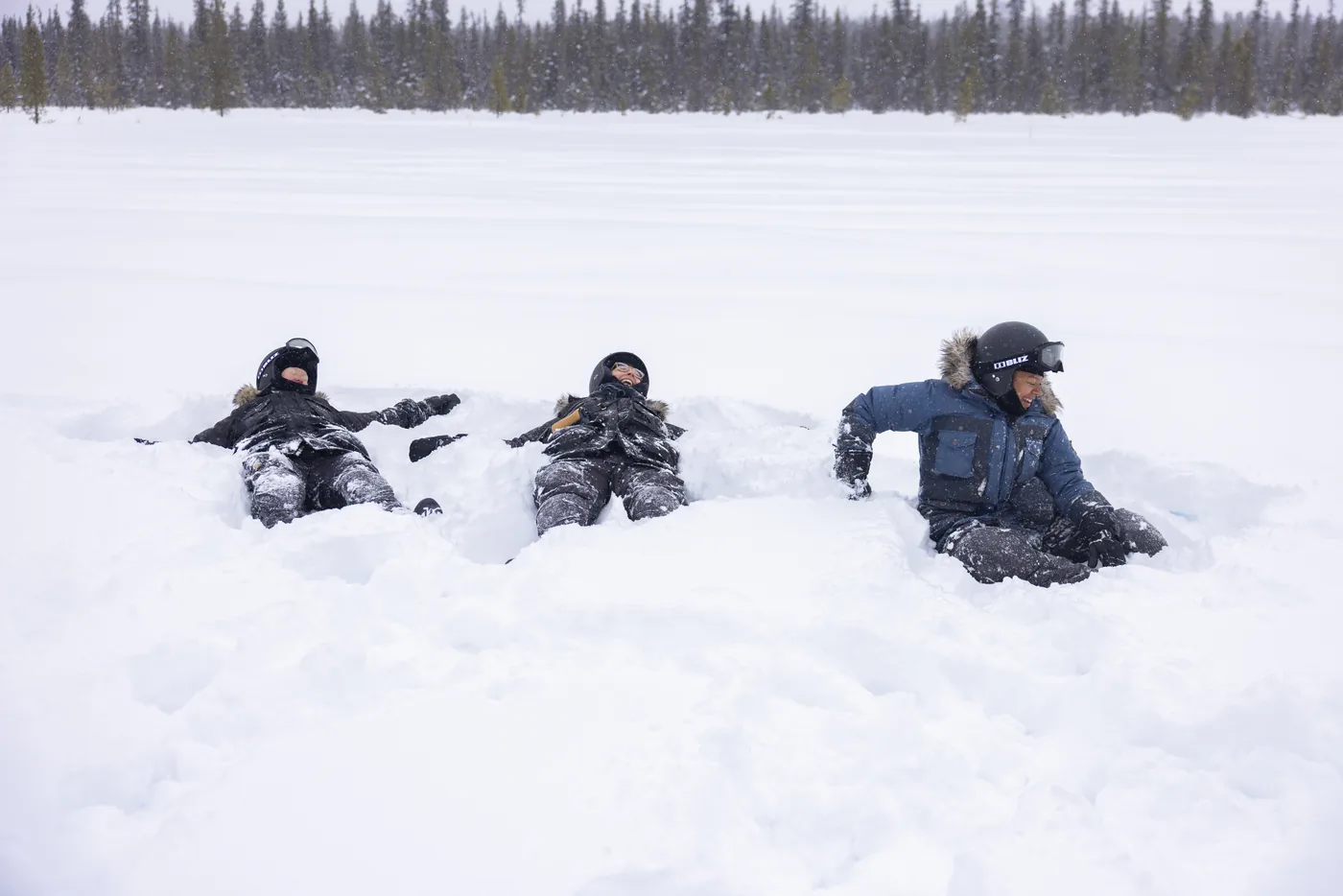 Guests lying back and laughing in deep snow beside a frozen lake