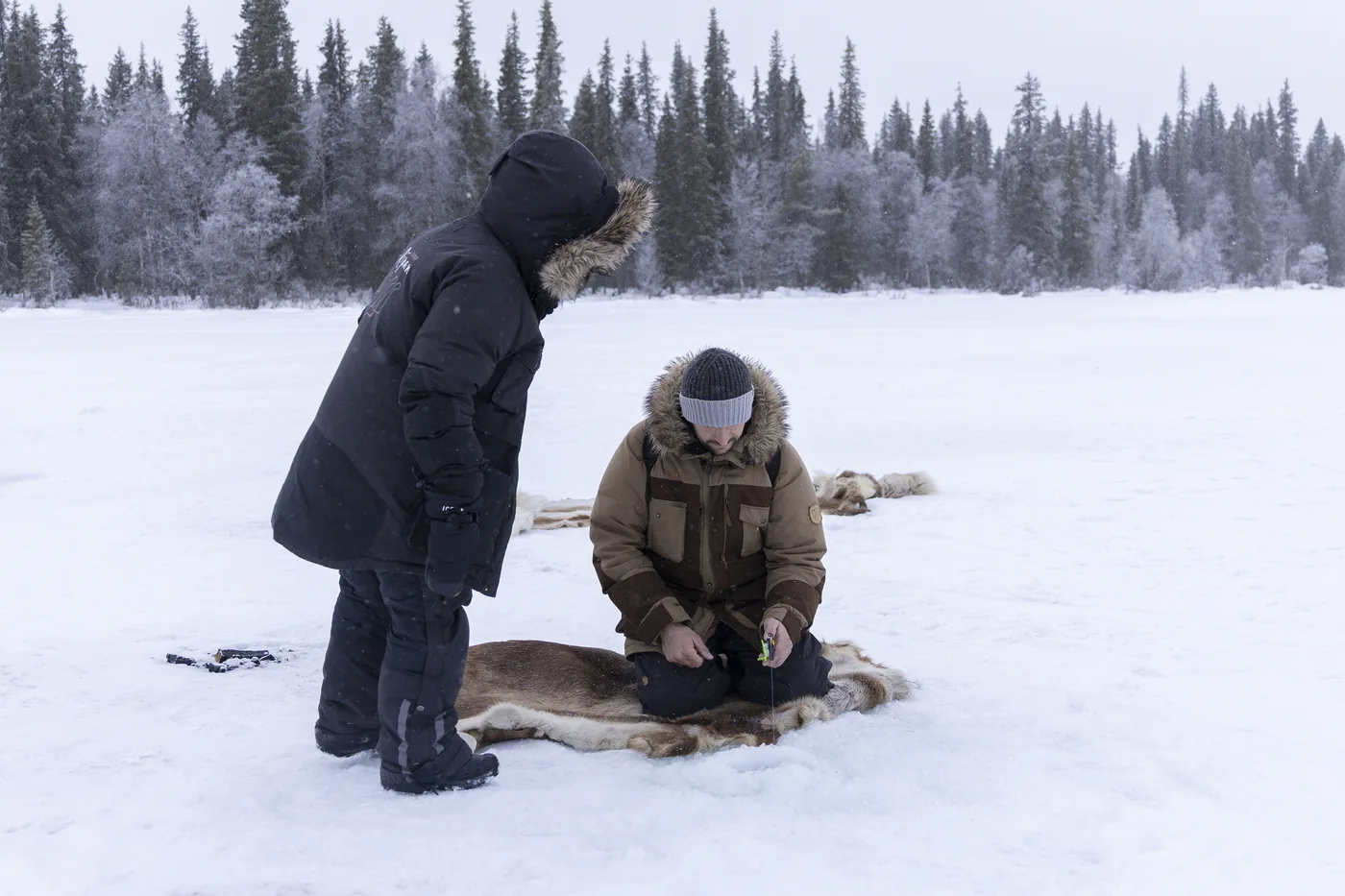 Guests ice fishing on reindeer hides in falling snow