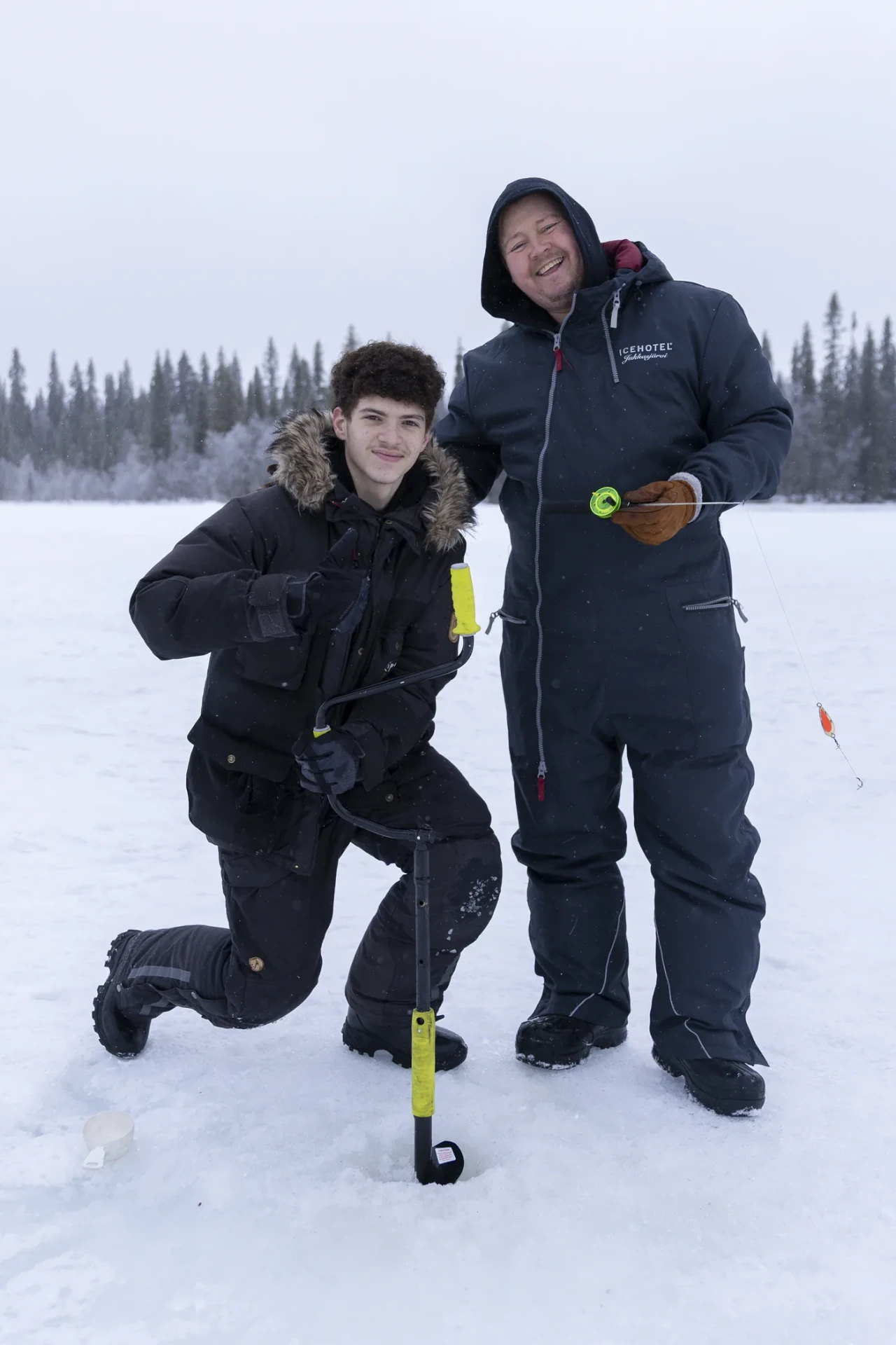 Guide and guest drilling an ice fishing hole on a frozen lake